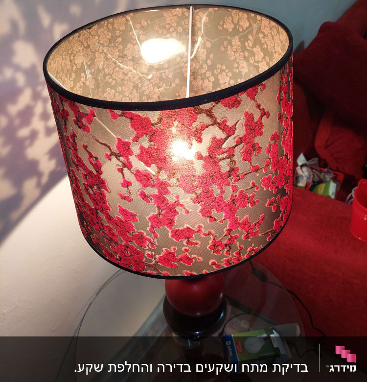 מנורה עם אהיל פרחוני ונורה חשמלית על שולחן זכוכית